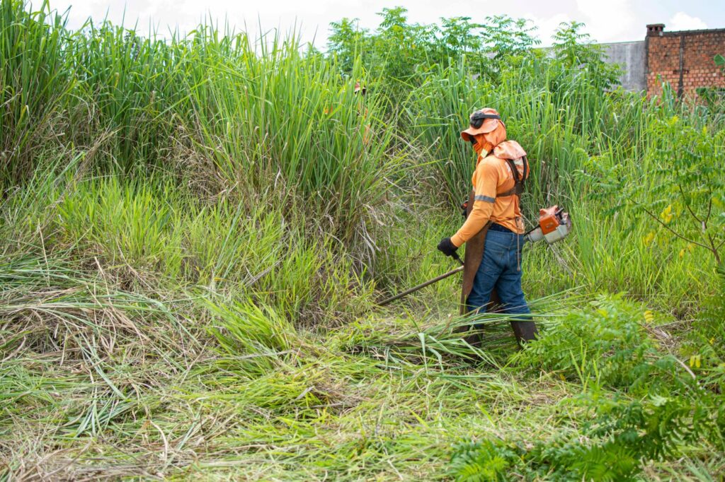 Profissional com EPI fazendo roçagem de terreno