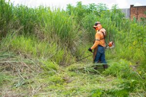 Profissional com EPI fazendo roçagem de terreno